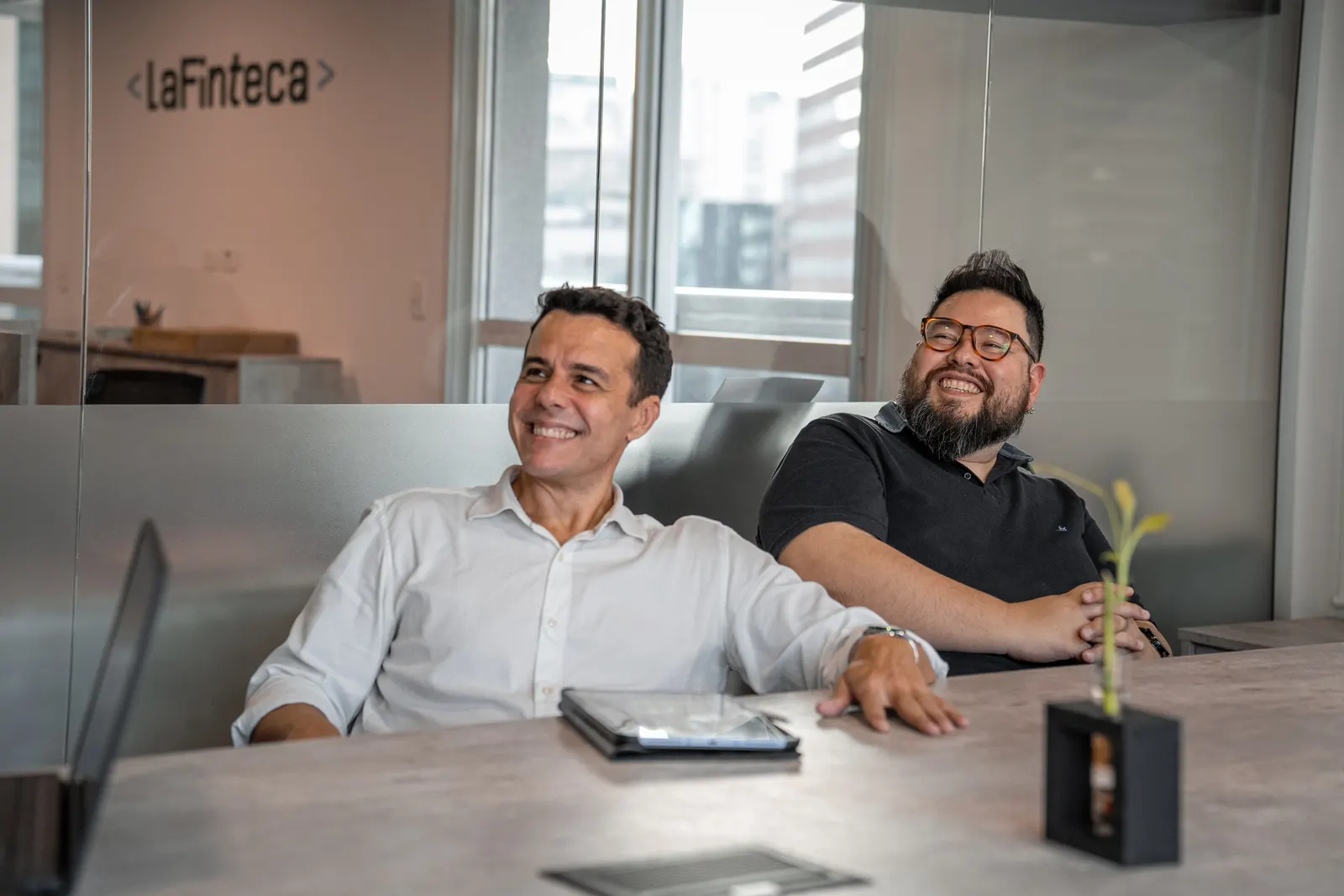 Two LaFinteca team members laughing together at a table in the office
